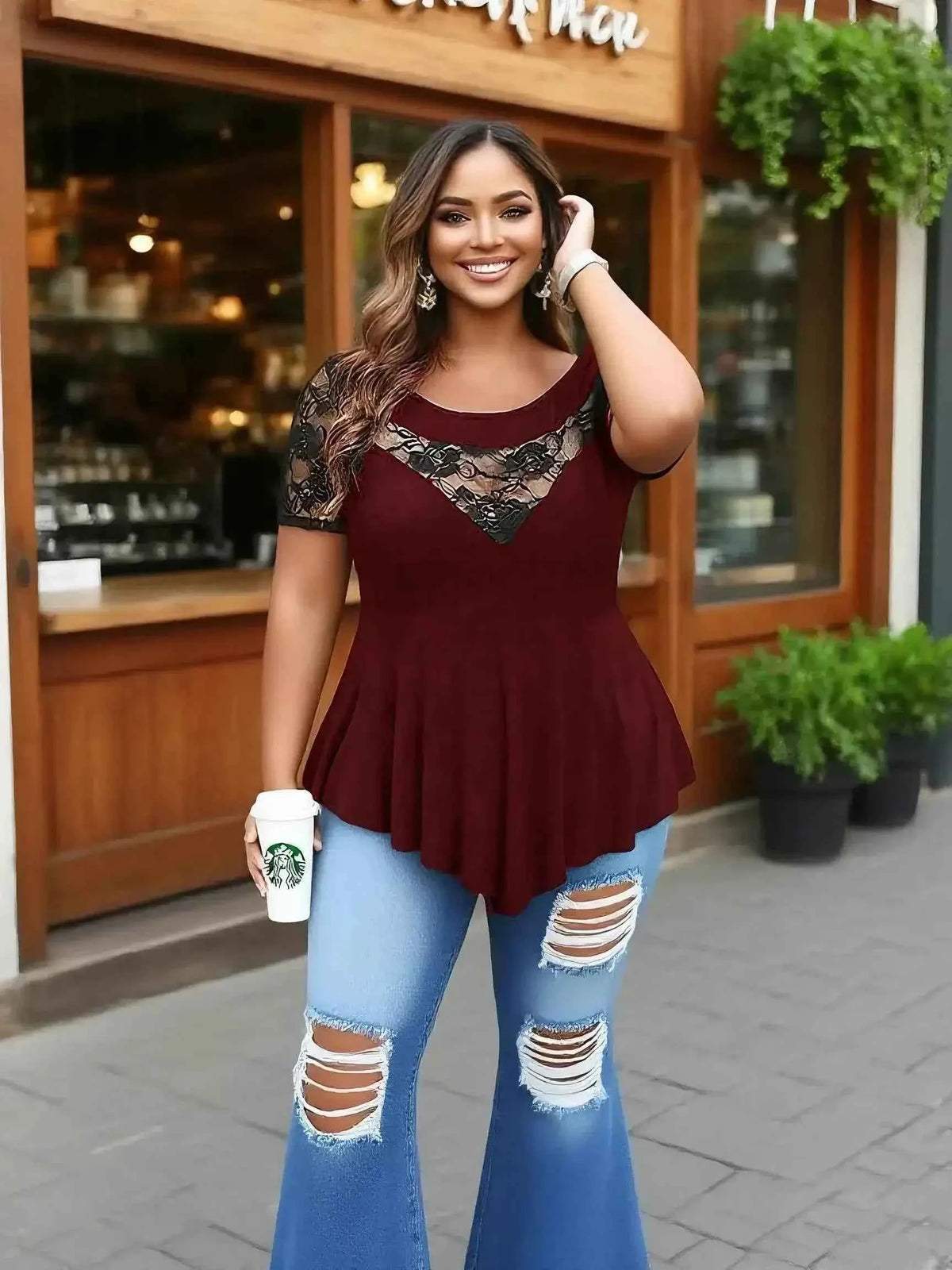 Top tunica pizzo taglie forti indossata da una donna sorridente con pantaloni flare in una caffetteria all'aperto.